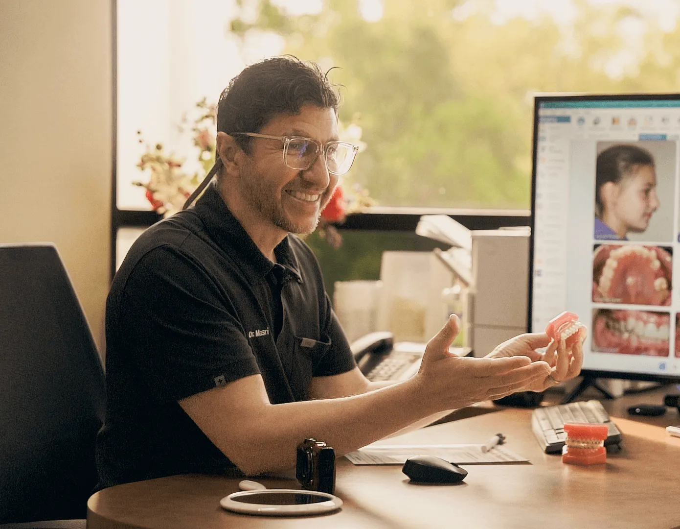 Dr. Nawaf Masri at his desk reviewing smile photos on a computer