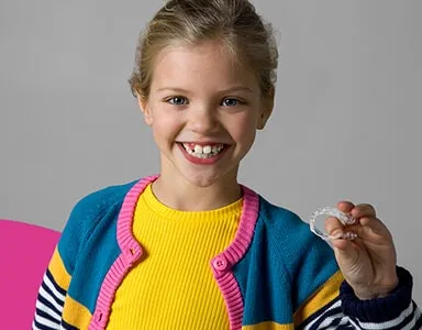 Smiling girl holding a clear aligner