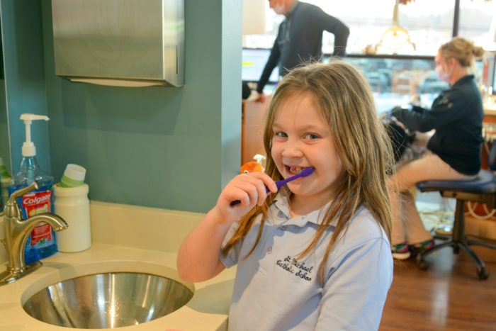 Young girl brushing her teeth at a sink in the orthodontic office