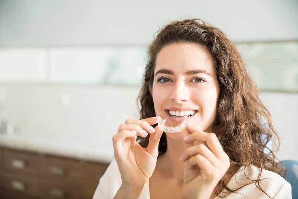 Smiling woman holding a clear Invisalign aligner