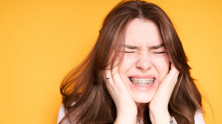 Young woman with braces holding her face in discomfort